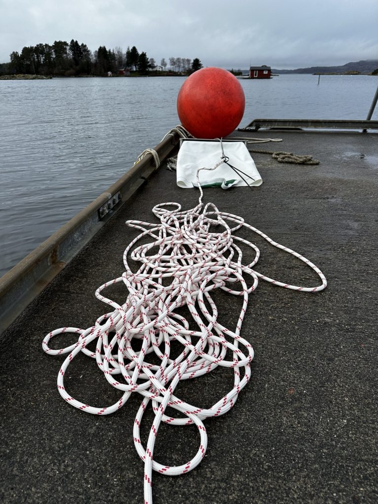 A small metal dredge, rope and a buoy on a dock