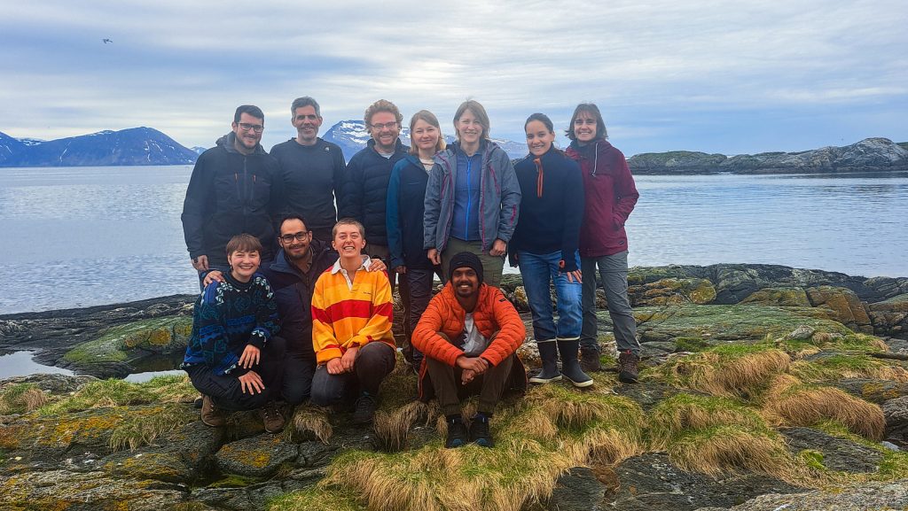 group photo of th eparticipants - 11 scientists in outdoor clothing standing in front of the ocean